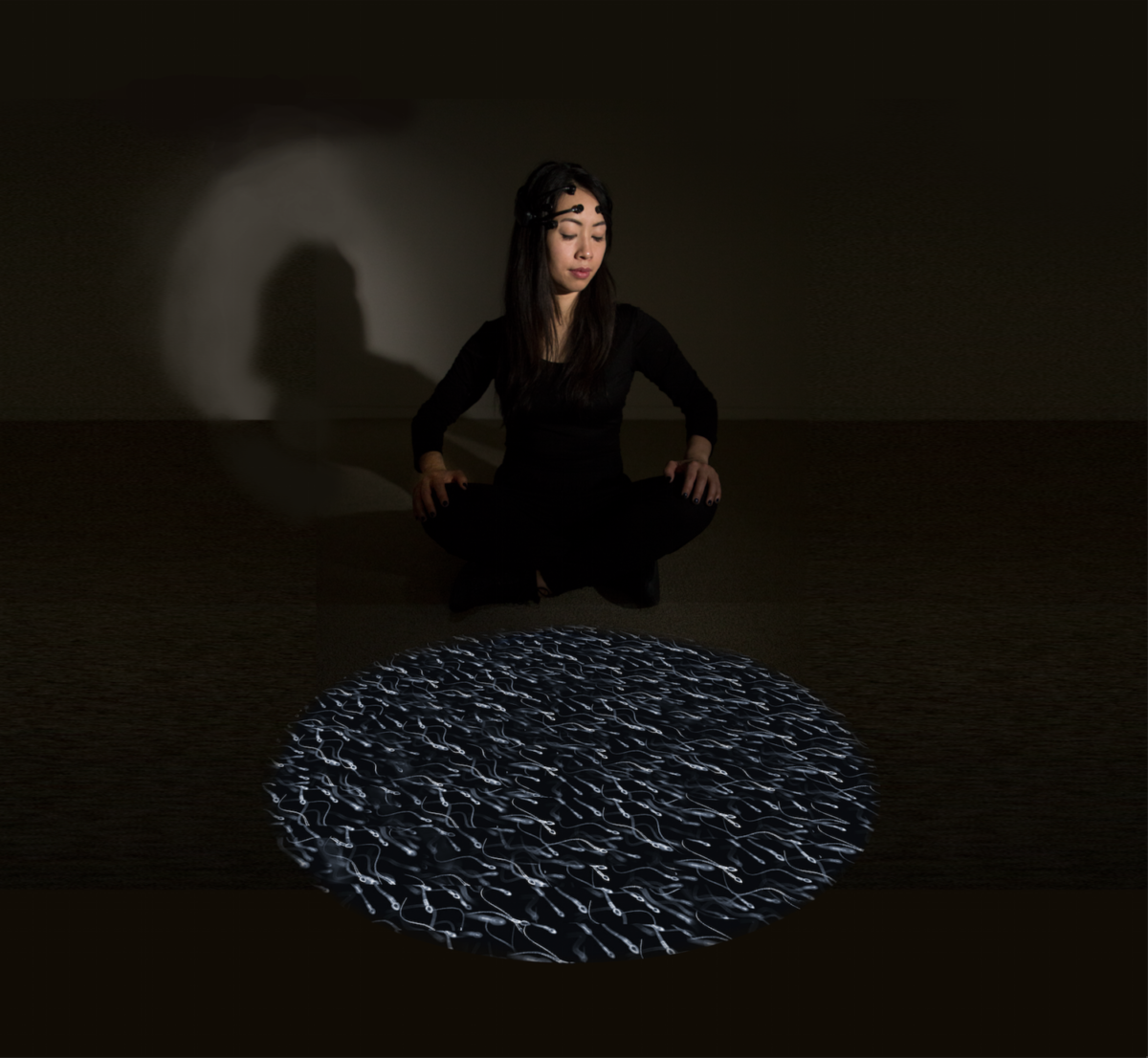 An artist sits in a dark room next to a spotlight projection.