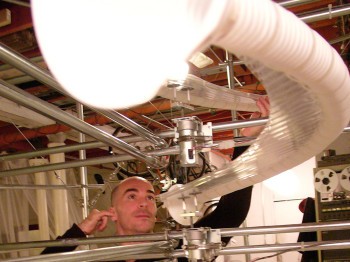 A man examines a large device made of a long plastic tube and metal bars