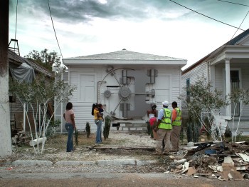 People stand in front of a house with a large complex lock covering the entire front door.