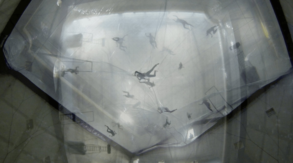 View from underneath of people lying on top of large clear sheets of plastic material.