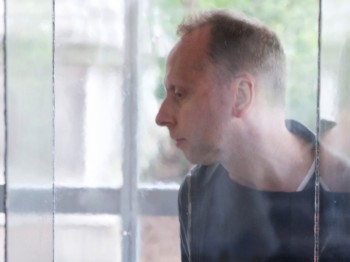 A man stands behind a glass box with a small black circular object