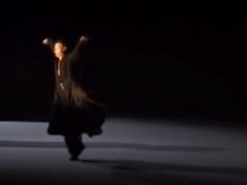 Blurry video still of a man in black robes dancing