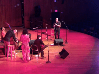 Five musicians perform on a large stage