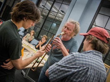 A man plays an instrument made out of a copper pipe while others look on.