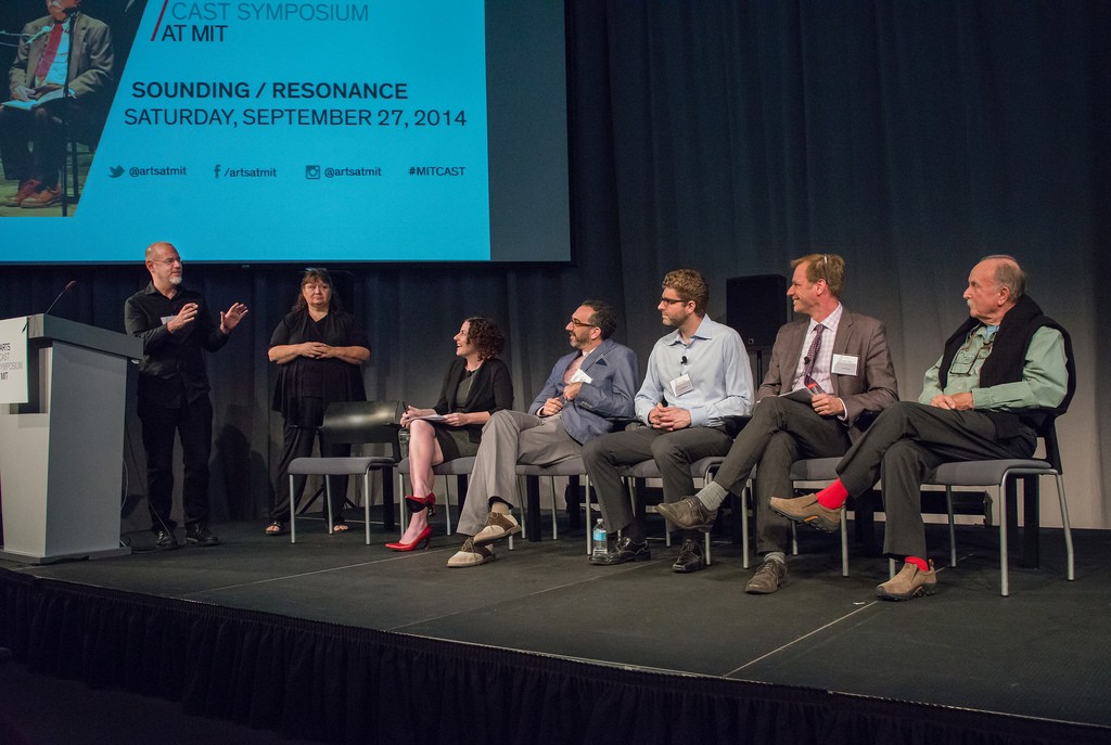 A panel of speakers on stage at a symposium.