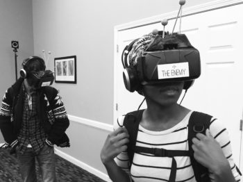 A participant in The Enemy wears a VR headset and holds onto the straps of a backpack containing equipment.