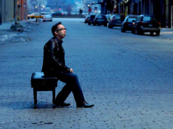 Joel Fan poses on a piano bench on a street.