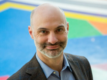 Auguston Rayo smiles into the camera while standing on the colorful Sol LeWitt floor.