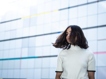 Woman in front of a colorful wall, turning to the side with her hair in motion.