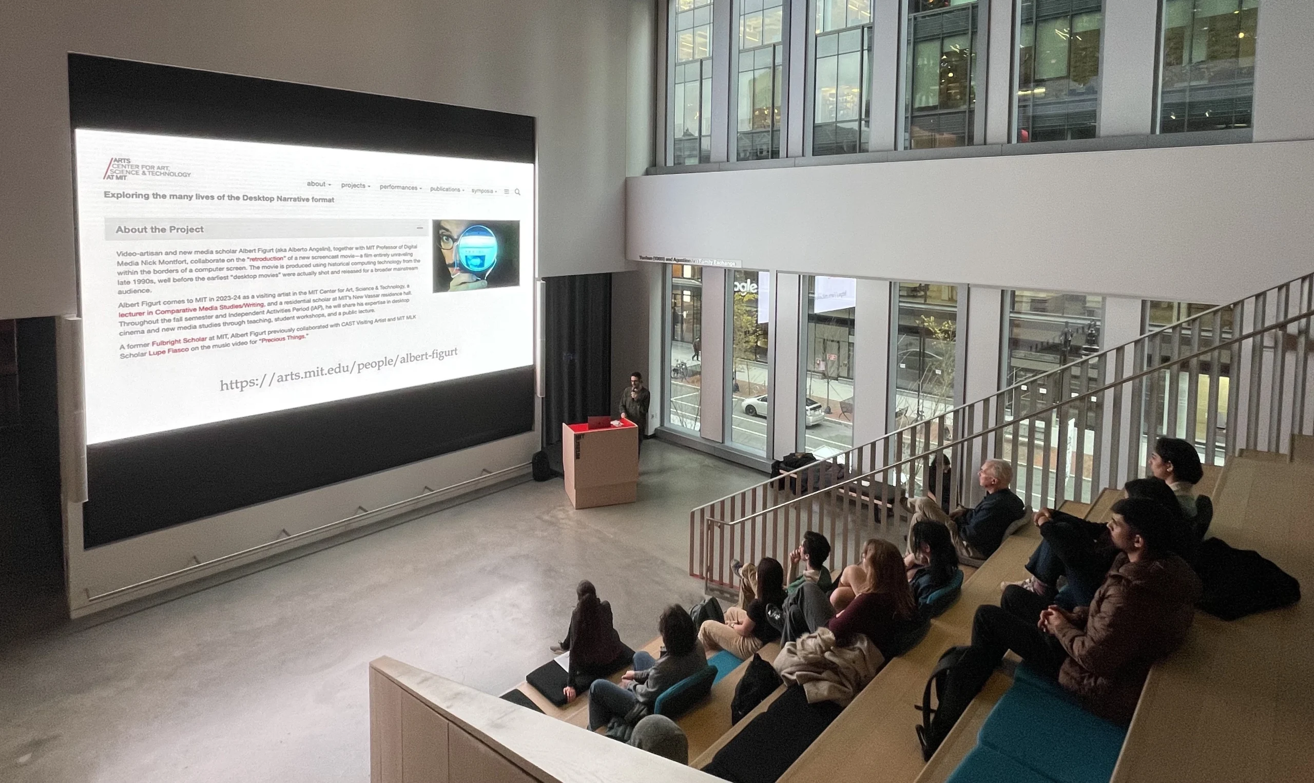 Albert Figurt presents his project on a big screen to a group seated on bleachers.