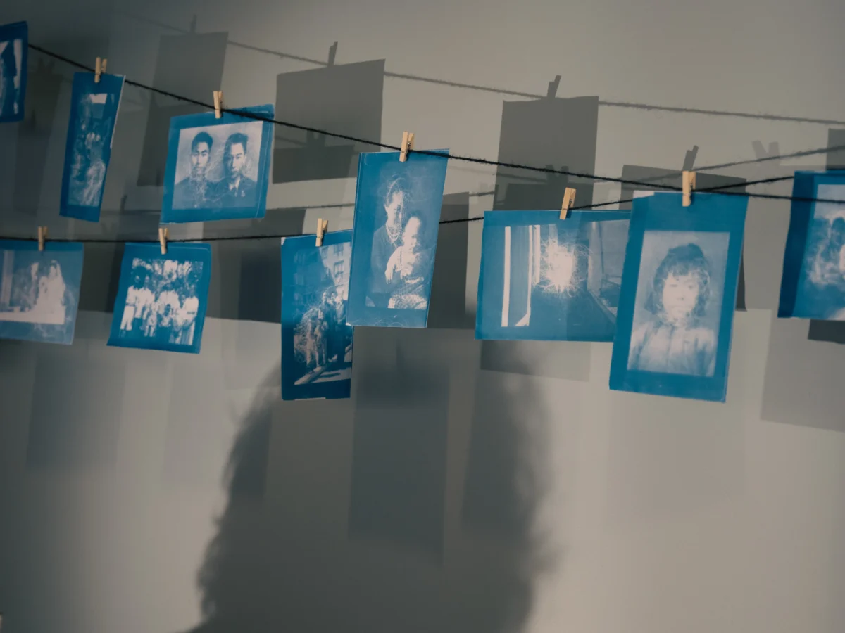 Blue and white printed images hang on a string forming a shadow against a white wall.