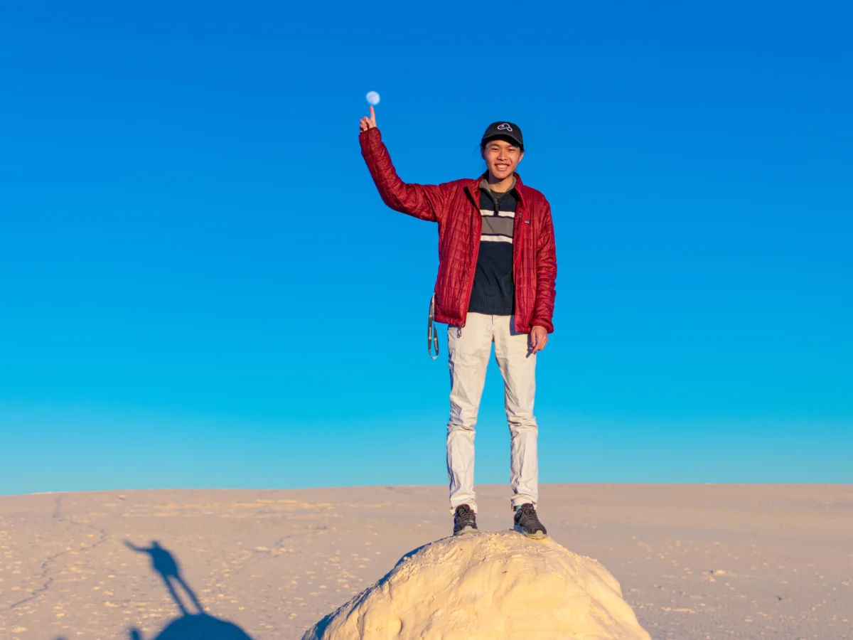 Alan Zhu posing on a rock making it look like one of their fingers is touching the moon.