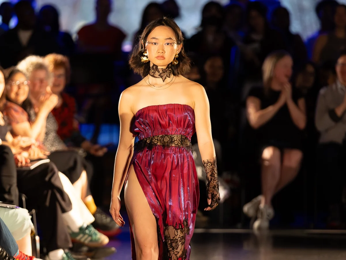 Model mid walk wearing a red dress and black necklace.