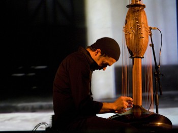 A man plucks strings on a large instrument made of wood and strings.