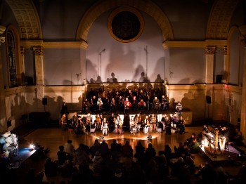 Musicians perform in an auditorium with shadowy lighting.